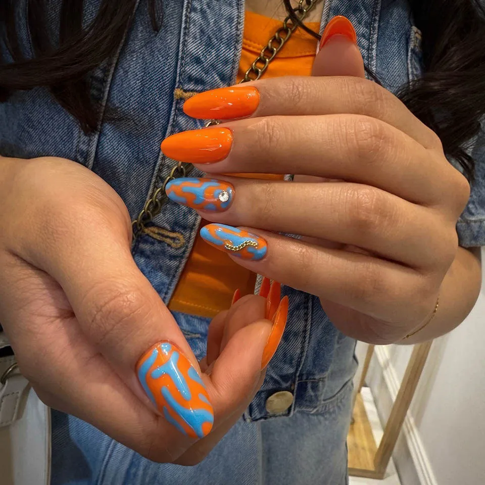 Long almond orange nails with blue abstract nail art and crystal accent
